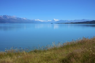 View over grassy banks to the mountain range behind the lake, Lake Pukaki Viewpoint, Pukaki,