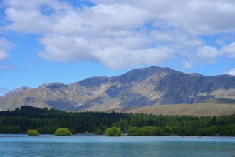Mountainous landscape with a lake in the foreground and wooded hills under a cloudy sky, Lake