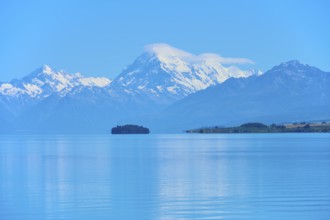 Large snow-capped mountain Mount Cook over a calm blue lake with a small island, Lake Pukaki