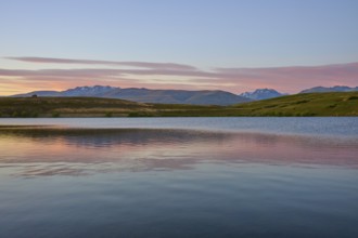 Clear lake with mountains in the background under a pink-blue morning sky, Lake McGregor, Tekapo,