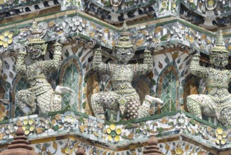 Demon figures (yaksha) supporting the central prang of Wat Arun decorated with colorful ceramic and