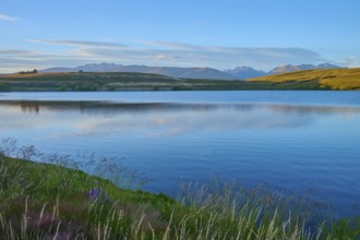 Calm lake with surrounding mountains and blue sky at sunset, Lake McGregor, Tekapo, Canterbury,
