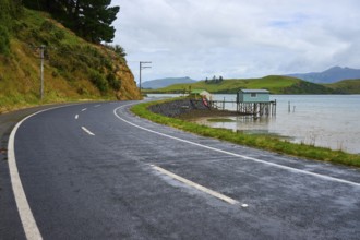 Road along the coast with a view of a distant cabin and green hills, Broad Bay, Dunedin, Otago,