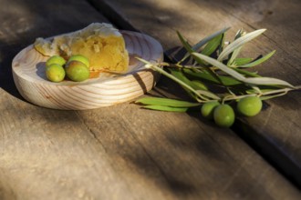Freshly picked green olives, an olive branch, and rustic bread on a wooden surface, suggesting