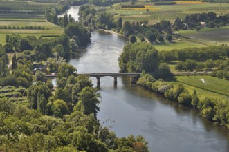 An aerial view of a serene river flowing under a bridge, surrounded by lush green fields and trees.