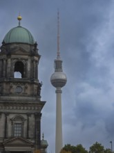 City view of Berlin Cathedral and TV Tower under grey, cloudy sky, contrasting mix of historic and