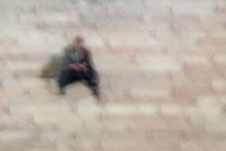 Abstract of a man sitting on stone steps and looking at a phone in his hands captured using ICM