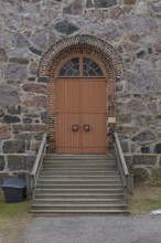 Closed old brown double doors with brick frame arch and window on top on a stone wall, Karjalohja,