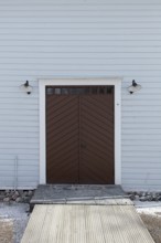 Closed old brown double doors with white frame and light blue board wall, Mustio, Finland