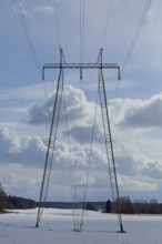 Steel tower with high voltage electric lines in cloudy winter weather with snow on the ground,