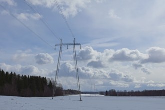 Steel tower with high voltage electric lines in cloudy winter weather with snow on the ground,