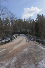 Gravel road on metal bridge over river Mustionjoki in winter, Junkarsborg, Finland