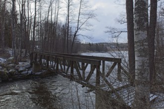 Old wood walking bridge over river Mustionjoki in cloudy winter weather, Junkarsborg, Finland