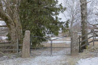 Closed old wrought iron gates mounted on stone gateposts to cemetery in winter, Degerby, Finland