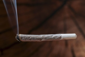 Burning joint producing smoke, highlighting drug use, cannabis culture, addiction, and illegal