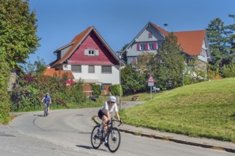 Country road with S-curve and two cyclists in Maria-Thann, Allgäu, Swabia, Bavaria, Germany