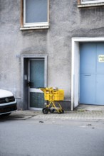 A yellow Deutsche Post delivery van stands in front of a grey façade between a front door and a