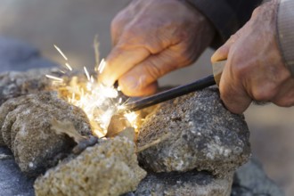 Bushcraft survivalist creating fire sparks with a ferro rod and cotton tinder, gathering heat