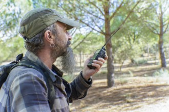 Man with beard and cap holding a walkie-talkie, communicating during an outdoor activity in a