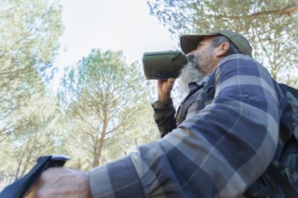 Man with beard and cap drinking water from a green canteen, hydrating during a trekking activity in