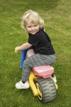 Blond Nordic girl, 3 years old, on a toy vehicle and looking back smiling in Ystad Municipality,