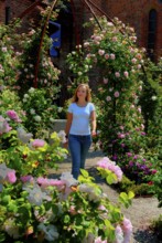 Blonde young beautiful woman walking among roses in the Rosary at the monastery in Ystad, Skåne