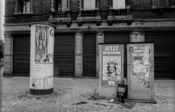 Germany, Berlin, 3.8.1992, advertising column and telephone booths, in front of closed shutters in