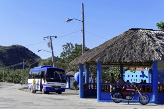 Baracoa, Cuba, Central America, bus and motorbike at a thatched roof bus stop in a rural area,