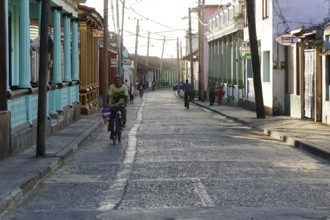 Baracoa, Cuba, Central America, narrow city street lively with cyclists and pedestrians in a