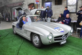 Silver 300 SL with open wing doors presents itself on the green carpet, interested audience in the
