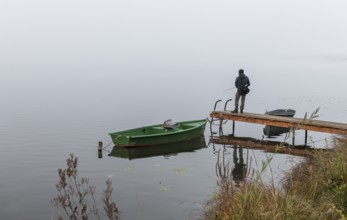 Fishermen on dock next to boats in fog at Hopfensee, Ostallgäu, Bavaria, Germany