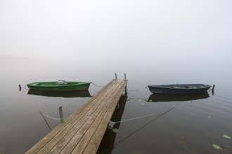 Two boats are moored on a wooden pier in fog, the atmosphere is calm and peaceful, Hopfensee,