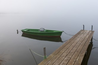 Single green boat on a wooden pier in fog, Hopfensee, Ostallgäu, Bavaria, Germany