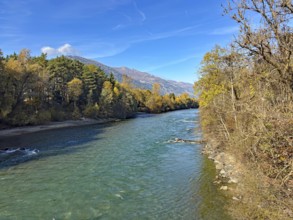 A quiet river surrounded by autumn trees and mountains under clear blue skies, Drau, Drauradweg,