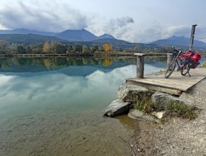 An idyllic lake with a bicycle on a jetty, surrounded by autumnal landscape and mountains, Drau,