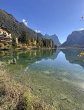 Clear water reflects the mountains and the house on the shore, Lake Toblach, Lake Dobbiaco, South