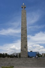 Tall stone column with symbolically decorated top under blue sky, memorial to 50 years of Soviet