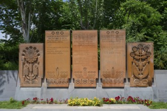 Stone monument with elaborate reliefs and surrounded by flowers, memorial plaques on Heroes' Alley