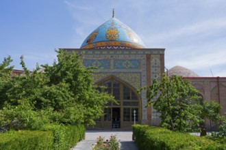 View of entrance to a mosque with blue dome and richly decorated portal, surrounded by garden, blue