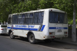 White police bus with Armenian lettering parked on the side of the road under shady trees, Yerevan,