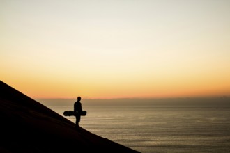 Silhouette of a sandboarder in Cerro Dragon at sunset, a sand dune located next to the city of
