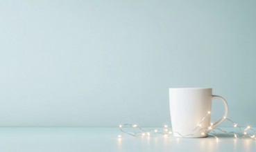 A white coffee cup sits on a table next to a string of lights. The scene is simple and calming,
