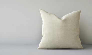 A white pillow with a pattern on it sits on a grey surface. The pillow is large and fluffy, and it