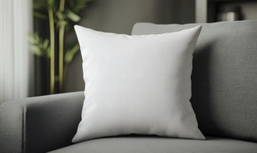 A white pillow sits on a gray couch. The pillow is the main focus of the image, and it is a