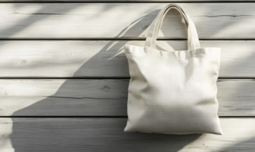 A white canvas bag is hanging on a wooden surface. The bag is empty and has a shadow on the wall
