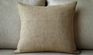 A tan pillow with a brown and white pattern sits on a couch. The pillow is the main focus of the
