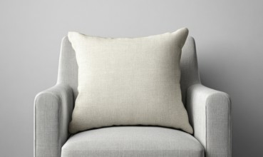 A white pillow on a gray chair. The pillow is large and has a textured surface. The chair is also
