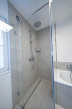 Floor-level shower with glass partition and rain shower head in calm shades of gray next to the