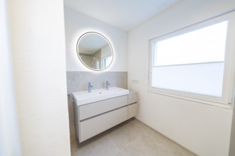 Bright bathroom with round illuminated mirror and double washbasin in front of subtle shades of