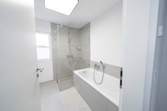 Modern bathroom with floor-level shower and tub in front of large format grey tiles and plenty of